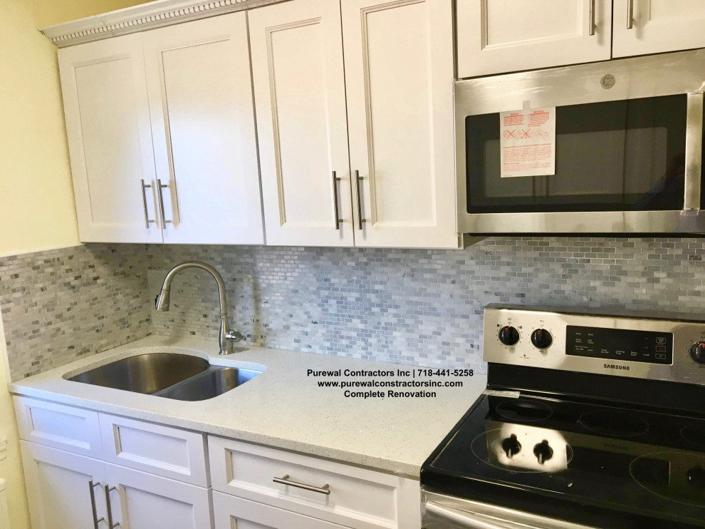 Mid-sized galley separate kitchen in New York with a triple-bowl sink, raised-panel cabinets, white cabinets, quartz benchtops, grey splashback, mosaic tile splashback, black appliances, cement tiles, grey floor and white benchtop.