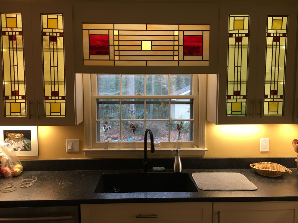 Photo of a mid-sized arts and crafts l-shaped eat-in kitchen in Atlanta with an undermount sink, recessed-panel cabinets, white cabinets, solid surface benchtops, multi-coloured splashback, glass tile splashback, stainless steel appliances, medium hardwood floors, no island, brown floor and black benchtop.