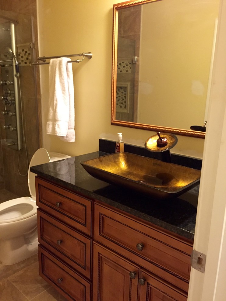 Mid-sized traditional 3/4 bathroom in DC Metro with raised-panel cabinets, medium wood cabinets, an alcove shower, a two-piece toilet, beige tile, ceramic tile, yellow walls, ceramic floors, a vessel sink, granite benchtops, beige floor and a hinged shower door.