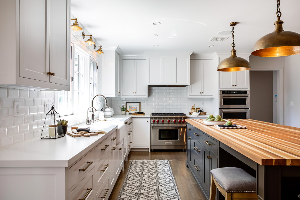 Mid-sized country l-shaped separate kitchen in Los Angeles with a farmhouse sink, shaker cabinets, white cabinets, white splashback, subway tile splashback, stainless steel appliances, medium hardwood floors, with island, brown floor, white benchtop and quartz benchtops.