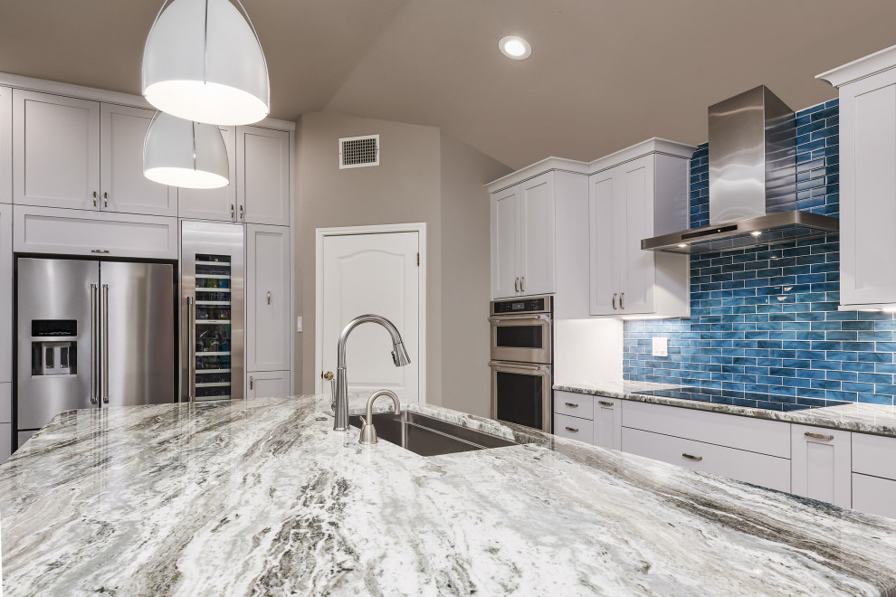 Example of a transitional porcelain tile and gray floor kitchen pantry design with a triple-bowl sink, shaker cabinets, white cabinets, quartzite countertops, blue backsplash, glass tile backsplash, stainless steel appliances, an island and gray countertops