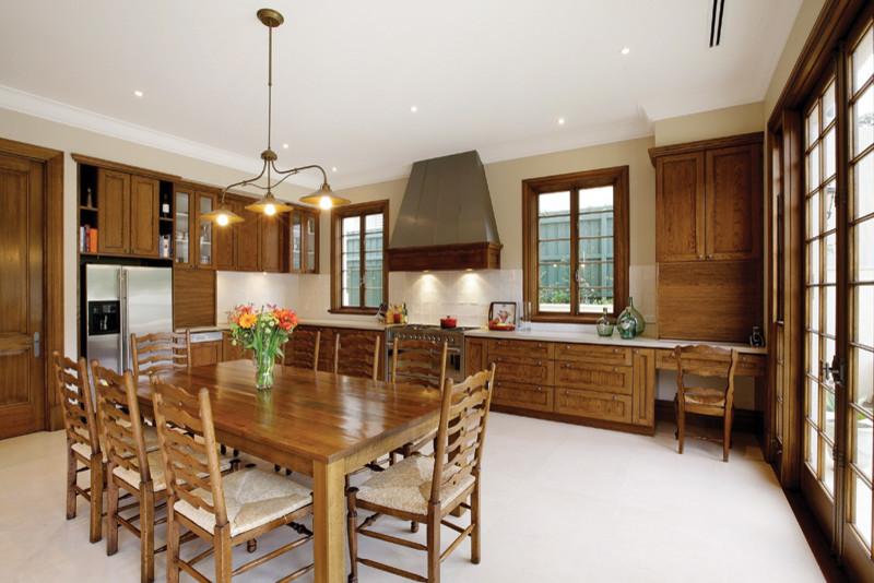Photo of a mid-sized traditional l-shaped kitchen in Melbourne with a drop-in sink, recessed-panel cabinets, medium wood cabinets, quartz benchtops, white splashback, subway tile splashback, stainless steel appliances and limestone floors.