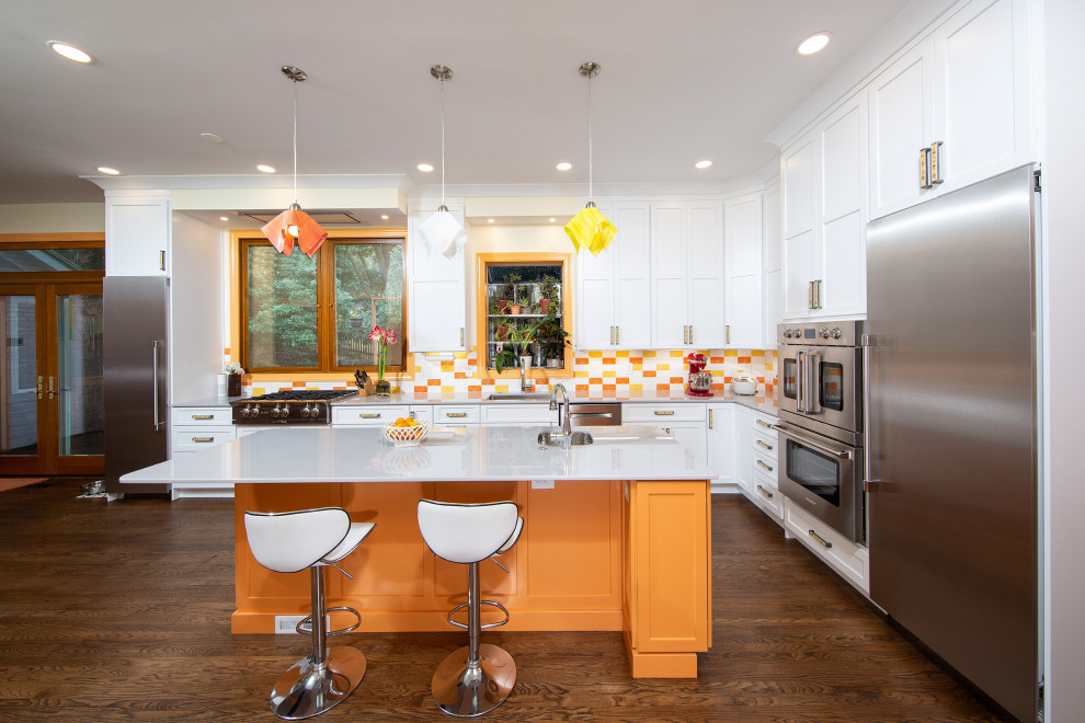 This is an example of an eclectic l-shaped kitchen in DC Metro with an undermount sink, shaker cabinets, white cabinets, multi-coloured splashback, stainless steel appliances, dark hardwood floors, with island, brown floor and grey benchtop.