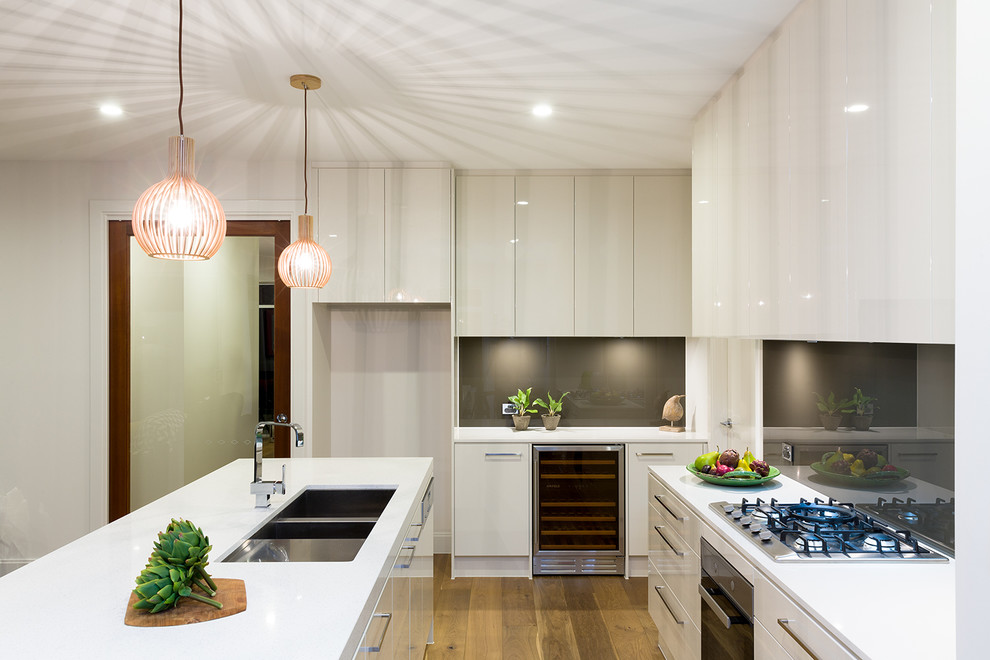 Large contemporary l-shaped kitchen pantry in Adelaide with an undermount sink, flat-panel cabinets, white cabinets, quartz benchtops, metallic splashback, glass sheet splashback, stainless steel appliances, light hardwood floors and with island.