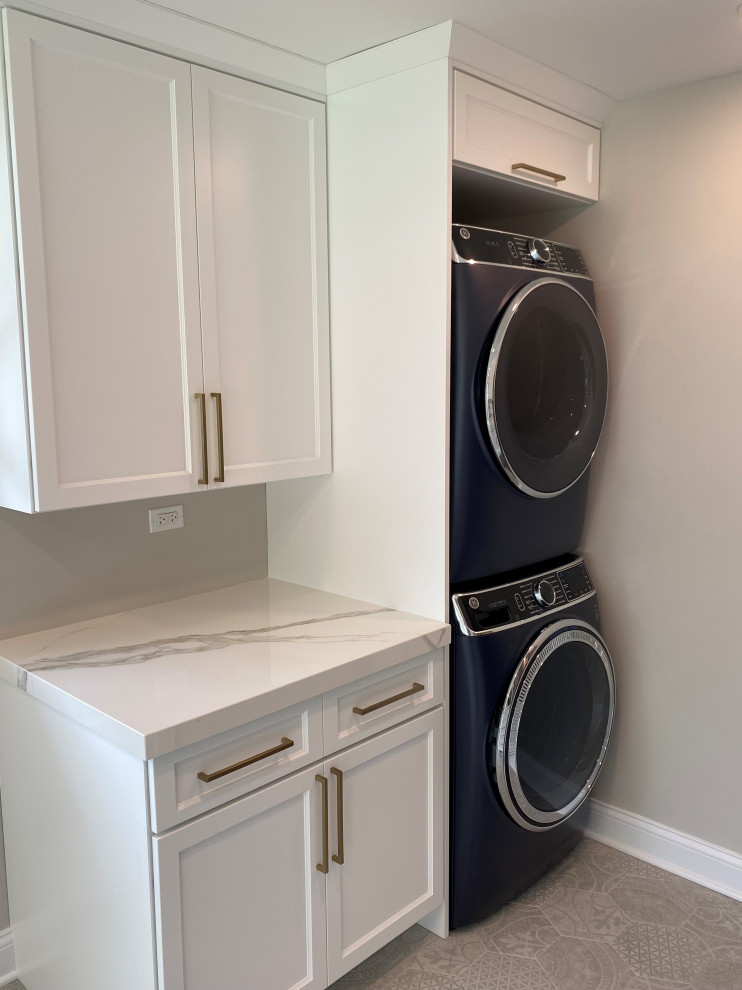 Photo of a mid-sized transitional l-shaped laundry room in Chicago with a farmhouse sink, flat-panel cabinets, grey cabinets, white splashback, stone tile splashback, medium hardwood floors, brown floor and white benchtop.