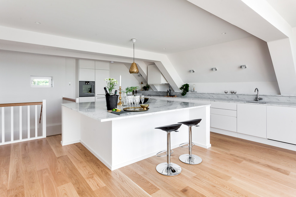 Photo of a large scandinavian single-wall kitchen in Stockholm with a single-bowl sink, flat-panel cabinets, white cabinets, marble benchtops, medium hardwood floors and with island.