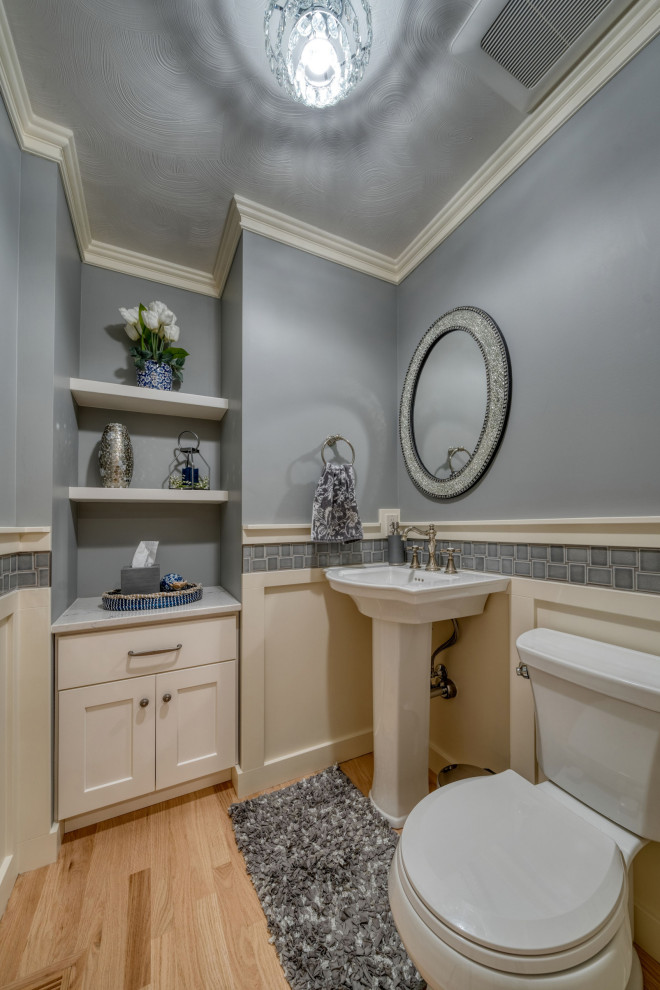 This is an example of a small farmhouse cloakroom in Other with a two-piece toilet, grey tiles, light hardwood flooring, a pedestal sink, grey worktops and wainscoting.