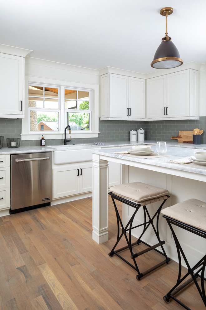 Inspiration for a mid-sized transitional l-shaped medium tone wood floor eat-in kitchen remodel in Charlotte with a farmhouse sink, white cabinets, marble countertops, gray backsplash, glass tile backsplash, stainless steel appliances, an island and white countertops