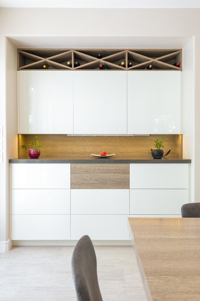 Photo of a mid-sized contemporary single-wall home bar in Orange County with flat-panel cabinets, white cabinets, quartz benchtops, grey benchtop, no sink, brown splashback and beige floor.