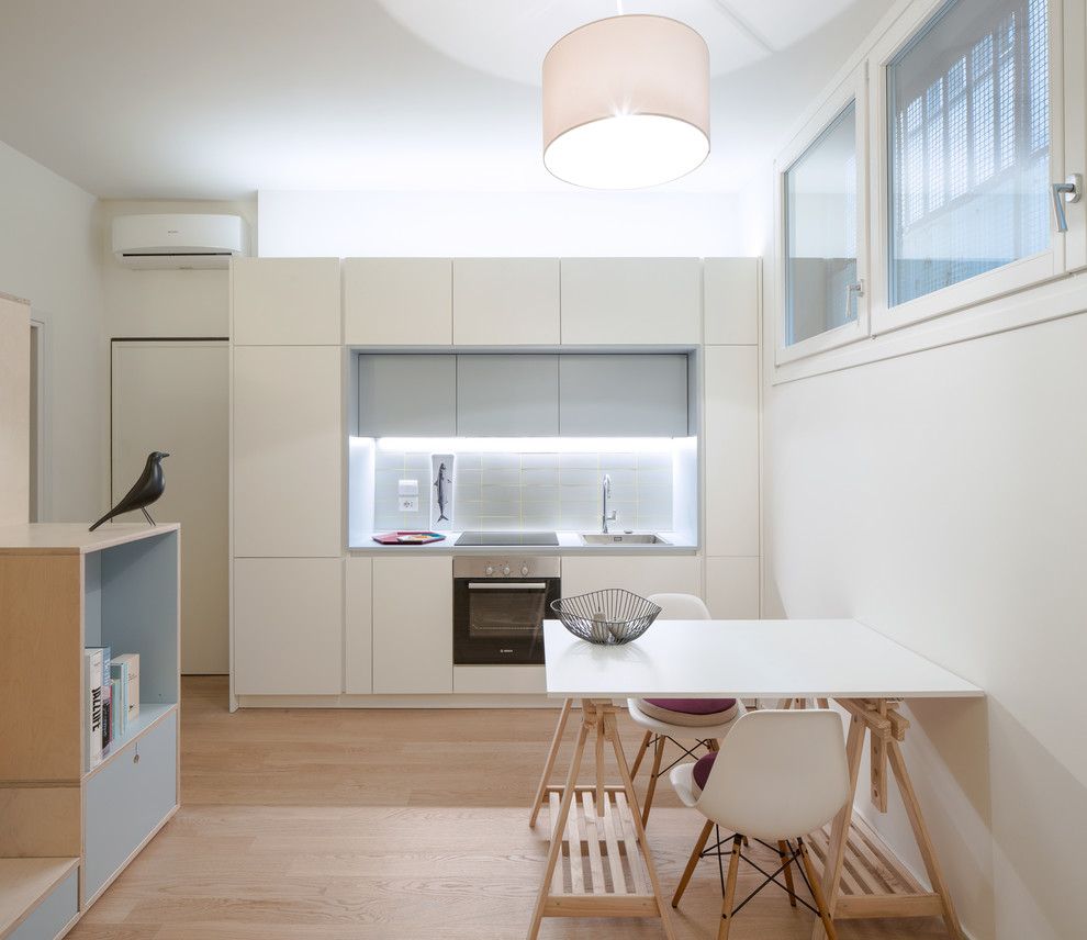 Small contemporary single-wall open plan kitchen in Milan with a single-bowl sink, flat-panel cabinets, white cabinets, laminate benchtops, grey splashback, ceramic splashback, stainless steel appliances, light hardwood floors, no island and beige floor.