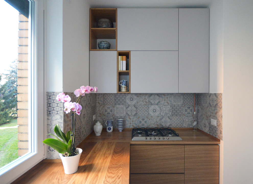 This is an example of a small contemporary l-shaped kitchen in Milan with flat-panel cabinets, light wood cabinets, wood benchtops, multi-coloured splashback and ceramic splashback.
