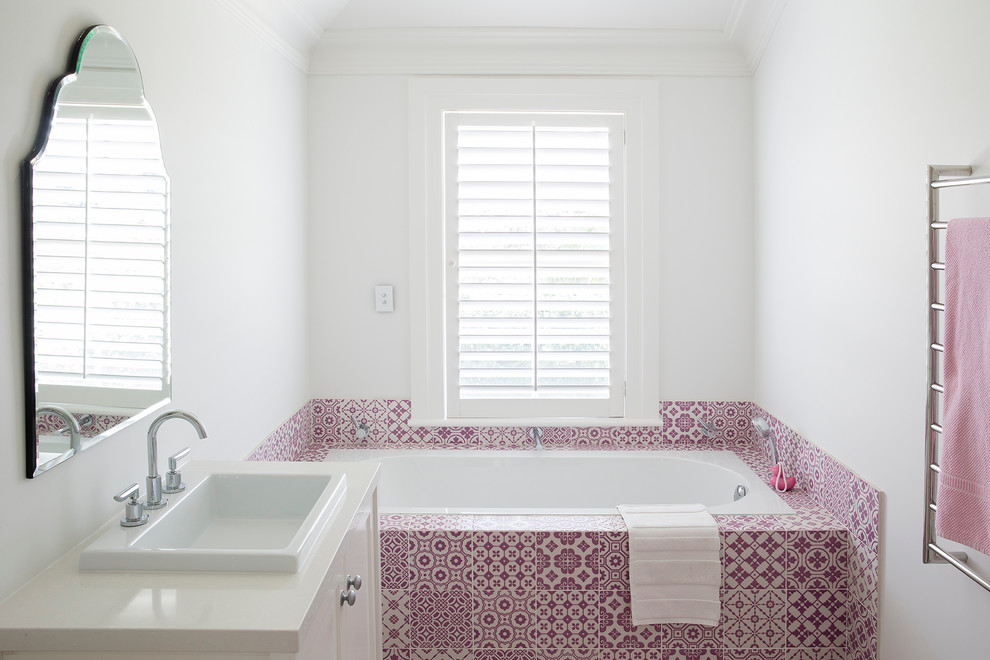 This is an example of a mid-sized mediterranean bathroom in Sydney with a drop-in sink, white cabinets, a drop-in tub, ceramic tile and white walls.