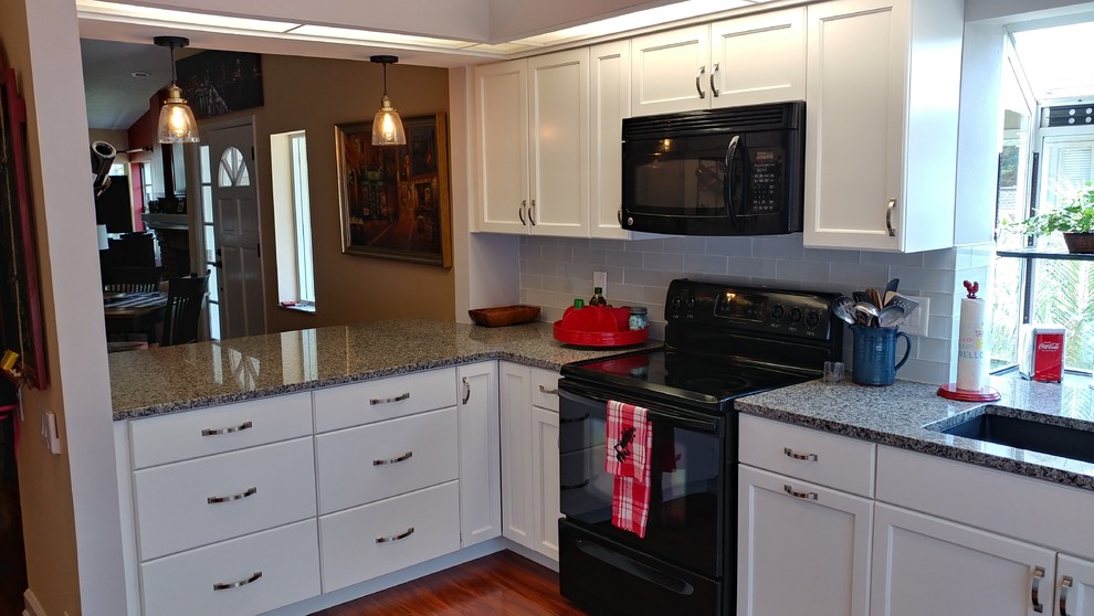 This is an example of a mid-sized traditional l-shaped separate kitchen in Tampa with a single-bowl sink, recessed-panel cabinets, white cabinets, granite benchtops, white splashback, glass tile splashback, black appliances, laminate floors, a peninsula and red floor.