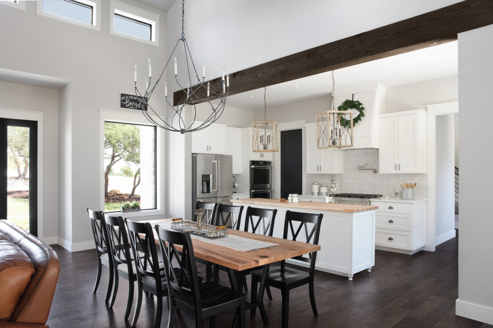 Country l-shaped open plan kitchen in Austin with white cabinets, grey splashback, stainless steel appliances, dark hardwood floors, with island, white benchtop and shaker cabinets.