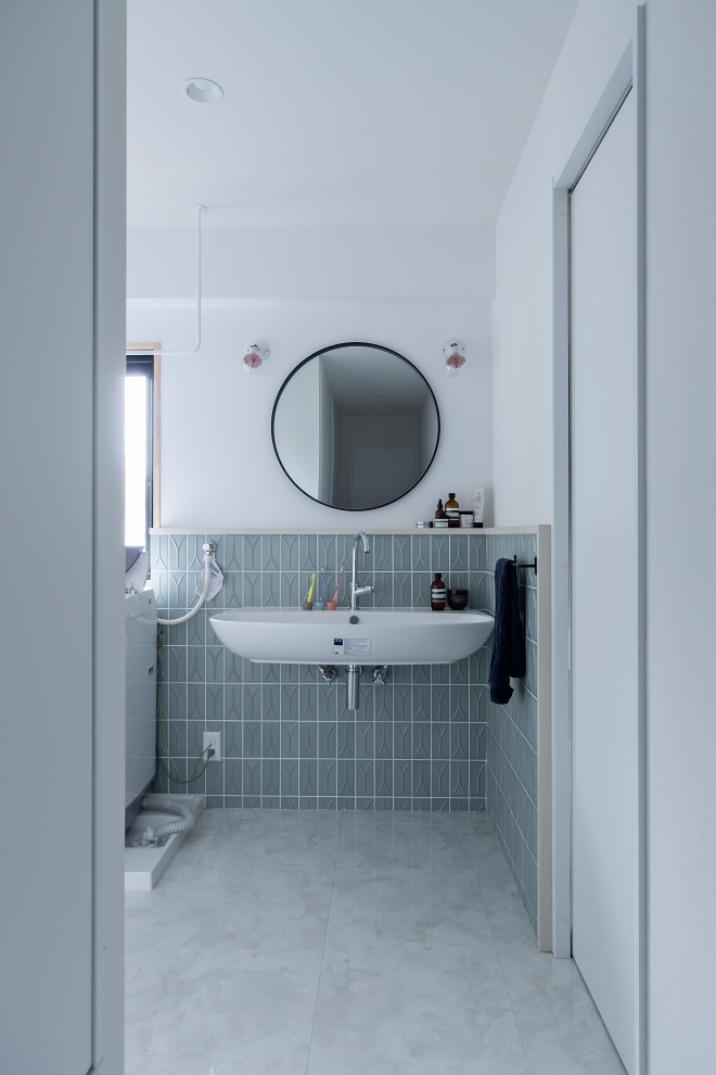 Midcentury powder room in Osaka with white cabinets, a one-piece toilet, blue tile, ceramic tile, green walls, medium hardwood floors, a wall-mount sink, brown floor and wallpaper.