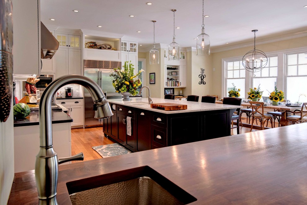 Example of a transitional medium tone wood floor eat-in kitchen design with an undermount sink, shaker cabinets, white cabinets, wood countertops, gray backsplash, subway tile backsplash, stainless steel appliances and an island
