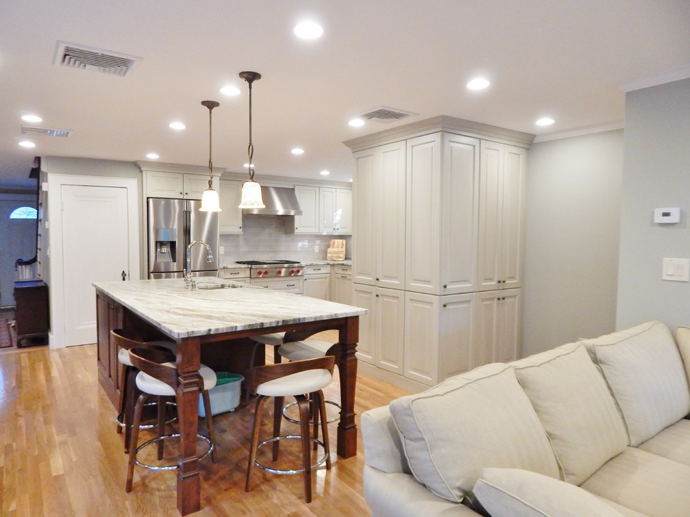 Example of a mid-sized transitional l-shaped light wood floor open concept kitchen design in Boston with an undermount sink, raised-panel cabinets, white cabinets, quartzite countertops, stainless steel appliances and an island