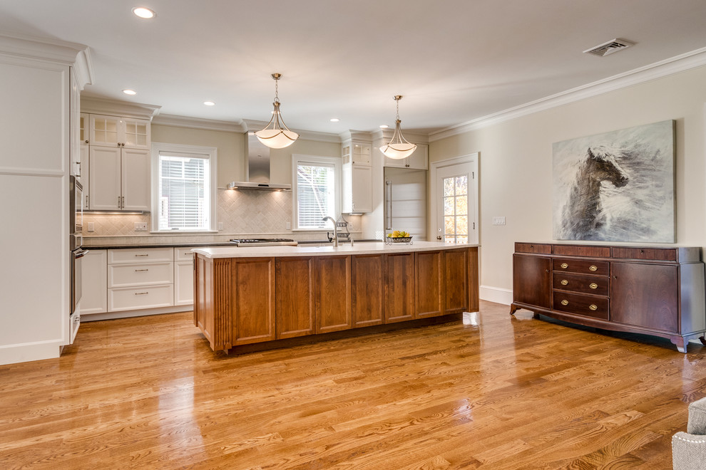 Open concept kitchen - mid-sized transitional l-shaped medium tone wood floor and brown floor open concept kitchen idea in Boston with a farmhouse sink, recessed-panel cabinets, white cabinets, soapstone countertops, beige backsplash, ceramic backsplash, stainless steel appliances and an island