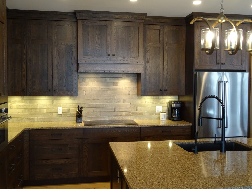 Example of a large transitional l-shaped light wood floor and brown floor kitchen pantry design with an undermount sink, shaker cabinets, medium tone wood cabinets, granite countertops, gray backsplash, stone tile backsplash, stainless steel appliances, an island and multicolored countertops