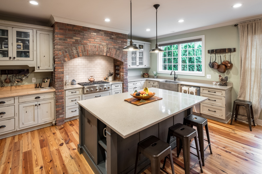 Large u-shaped kitchen in Detroit with distressed cabinets, quartz benchtops, stainless steel appliances, with island, brown floor, white benchtop, a farmhouse sink, beaded inset cabinets, white splashback, subway tile splashback and medium hardwood floors.