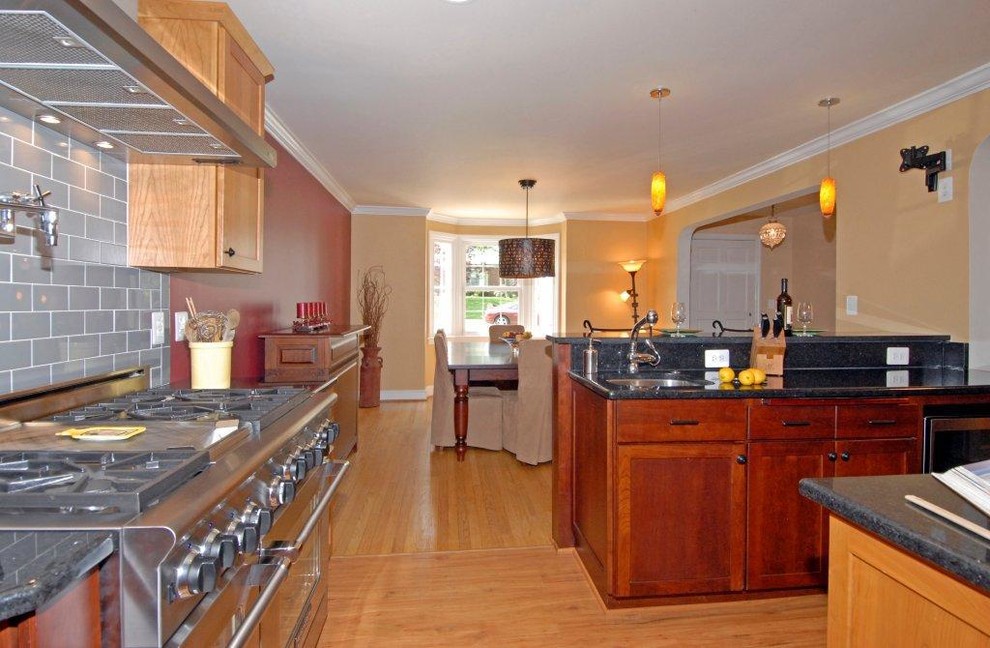 Large transitional u-shaped medium tone wood floor eat-in kitchen photo in DC Metro with a farmhouse sink, shaker cabinets, medium tone wood cabinets, granite countertops, gray backsplash, subway tile backsplash, stainless steel appliances and a peninsula