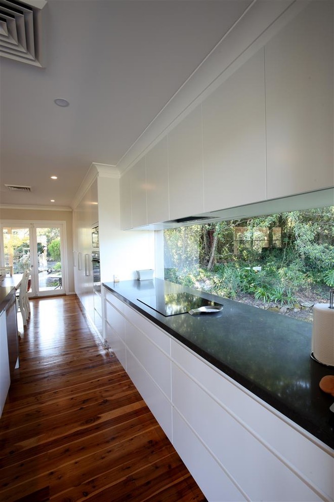 This is an example of a mid-sized contemporary single-wall eat-in kitchen in Sydney with a double-bowl sink, flat-panel cabinets, white cabinets, marble benchtops, window splashback, stainless steel appliances, medium hardwood floors and with island.