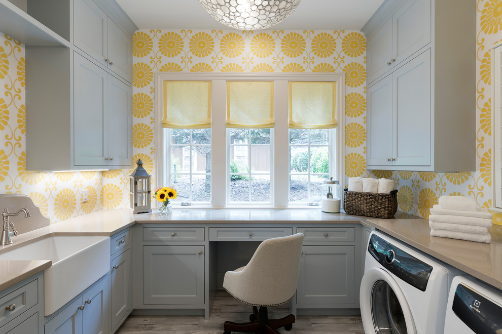 Design ideas for a beach style u-shaped dedicated laundry room in Minneapolis with a farmhouse sink, grey cabinets, yellow walls, light hardwood floors, a side-by-side washer and dryer, beige floor and shaker cabinets.