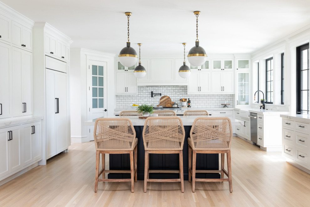 This is an example of a large country u-shaped kitchen in Sacramento with a farmhouse sink, shaker cabinets, white cabinets, quartz benchtops, white splashback, subway tile splashback, light hardwood floors, multiple islands and white benchtop.