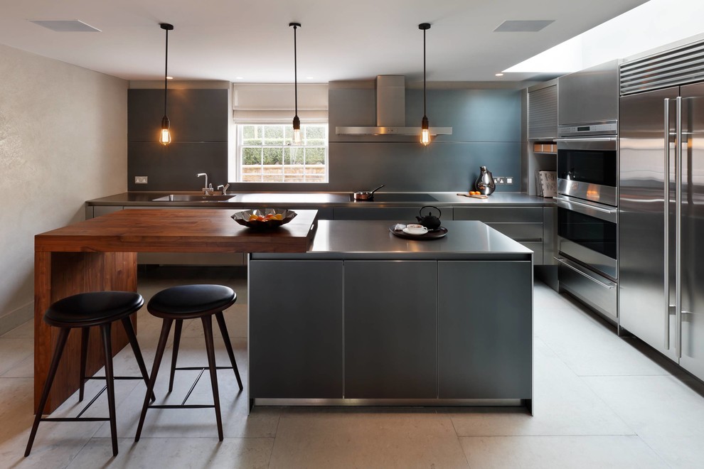 Mid-sized contemporary l-shaped eat-in kitchen in London with an integrated sink, flat-panel cabinets, stainless steel cabinets, stainless steel benchtops, metallic splashback, stainless steel appliances, limestone floors and with island.