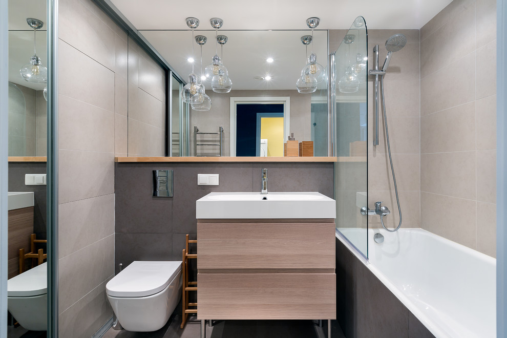Inspiration for a small scandinavian master bathroom in Saint Petersburg with flat-panel cabinets, light wood cabinets, an alcove tub, a shower/bathtub combo, a wall-mount toilet, gray tile, porcelain tile, porcelain floors, grey floor and an integrated sink.