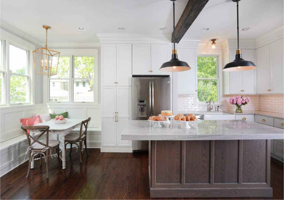 This is an example of a large transitional l-shaped eat-in kitchen in Chicago with a farmhouse sink, quartzite benchtops, white splashback, ceramic splashback, stainless steel appliances, with island, brown floor, grey benchtop, recessed-panel cabinets, white cabinets and dark hardwood floors.