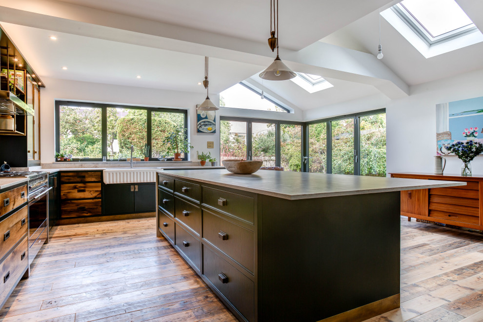 Mid-sized eclectic l-shaped eat-in kitchen in Cambridgeshire with a double-bowl sink, beaded inset cabinets, green cabinets, solid surface benchtops, white splashback, ceramic splashback, black appliances, medium hardwood floors, with island, brown floor, multi-coloured benchtop and vaulted.