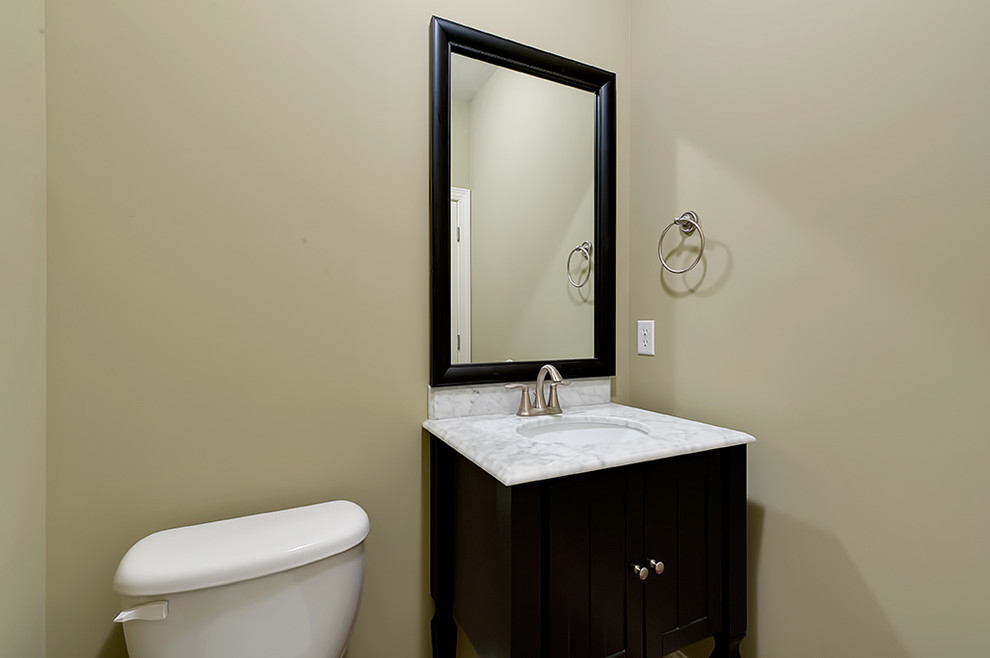 Example of a transitional powder room design with a drop-in sink, flat-panel cabinets, black cabinets, marble countertops, a one-piece toilet and beige walls
