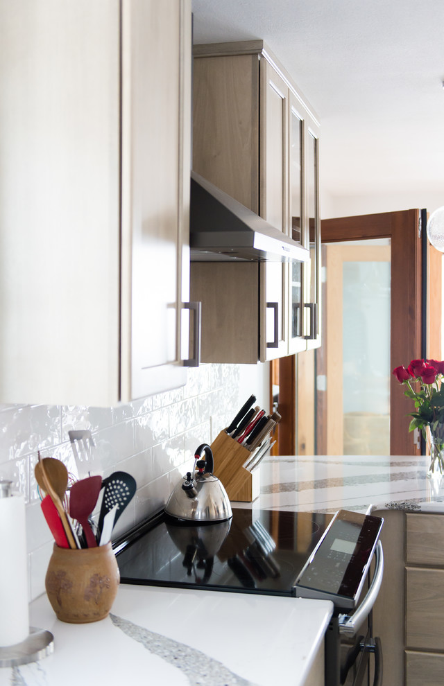 Inspiration for a mid-sized transitional u-shaped vinyl floor and brown floor enclosed kitchen remodel with an undermount sink, flat-panel cabinets, beige cabinets, quartz countertops, white backsplash, subway tile backsplash, black appliances, a peninsula and white countertops
