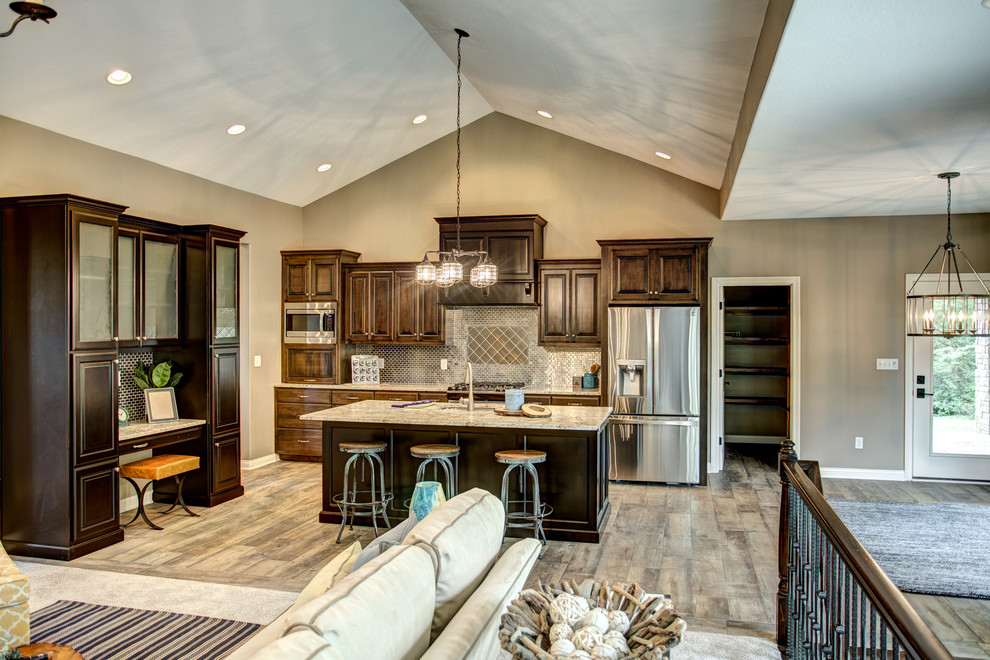 Open concept kitchen - mid-sized transitional single-wall medium tone wood floor and gray floor open concept kitchen idea with an undermount sink, raised-panel cabinets, dark wood cabinets, granite countertops, metallic backsplash, metal backsplash, stainless steel appliances and an island
