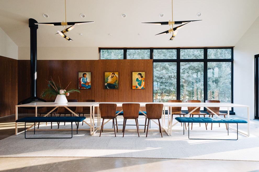 This is an example of a midcentury dining room in Louisville with white walls, concrete floors, a hanging fireplace and grey floor.
