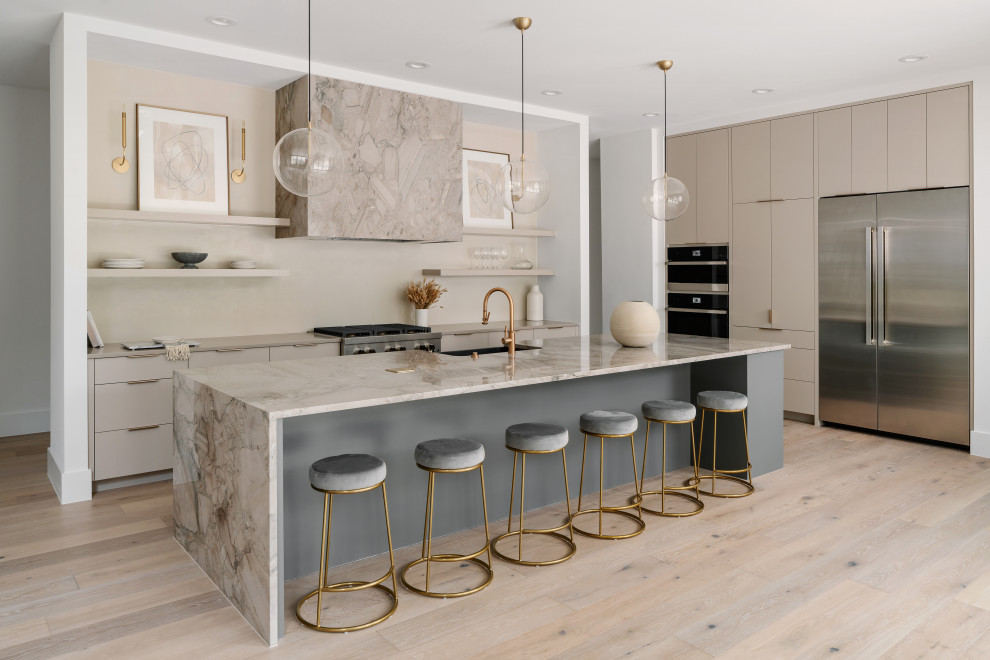 This is an example of a contemporary u-shaped eat-in kitchen in Austin with a farmhouse sink, flat-panel cabinets, beige cabinets, marble benchtops, beige splashback, stainless steel appliances, light hardwood floors, with island, beige floor and multi-coloured benchtop.