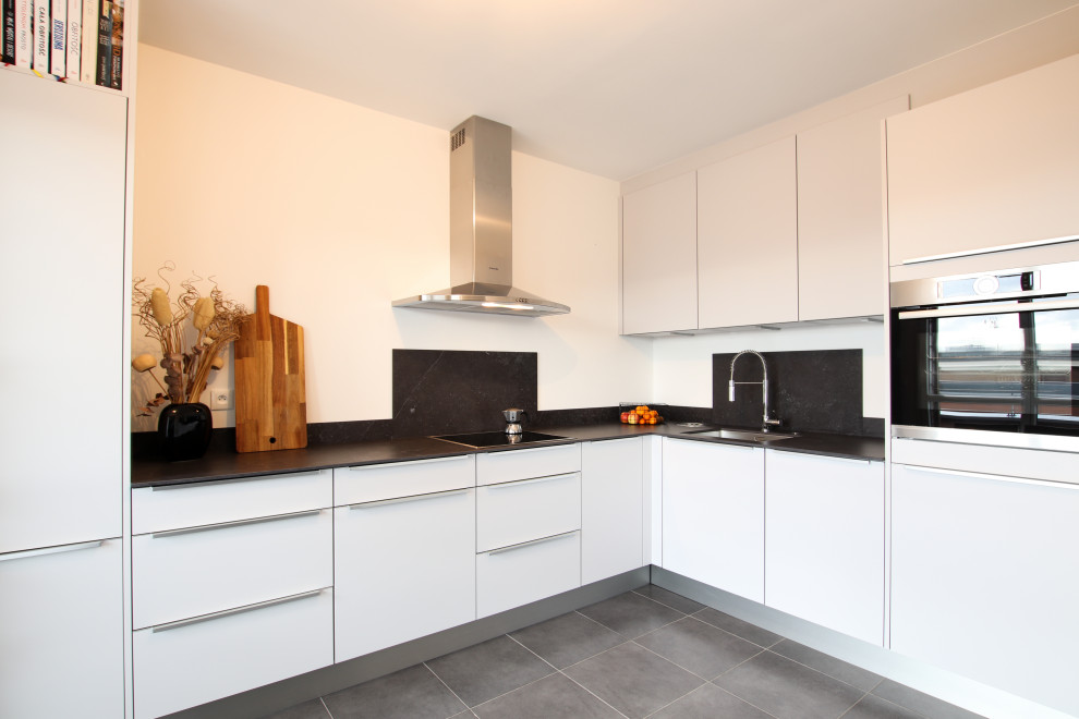 Inspiration for a mid-sized contemporary l-shaped separate kitchen in Lyon with a single-bowl sink, grey cabinets, granite benchtops, black splashback, ceramic splashback, stainless steel appliances, ceramic floors, no island, grey floor and black benchtop.