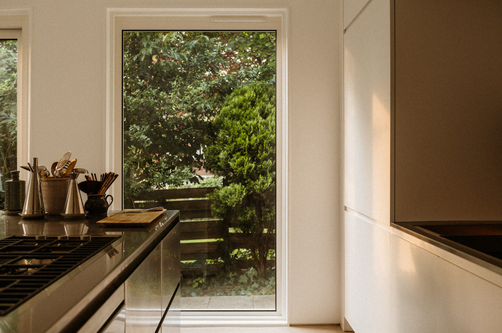 Modern inredning av ett mellanstort linjärt kök och matrum, med en integrerad diskho, släta luckor, skåp i rostfritt stål, bänkskiva i rostfritt stål, integrerade vitvaror, betonggolv och en köksö