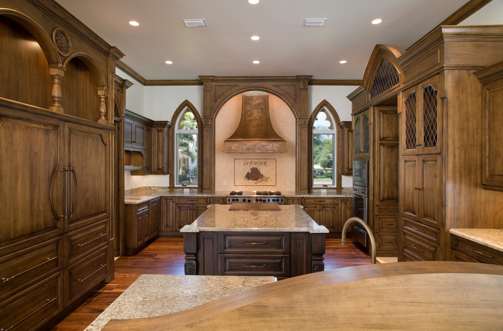 Photo of an expansive traditional u-shaped open plan kitchen in Orlando with a farmhouse sink, raised-panel cabinets, dark wood cabinets, granite benchtops, beige splashback, stone slab splashback, panelled appliances, medium hardwood floors, with island and brown floor.