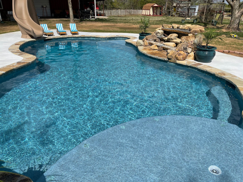 Immagine di una piscina naturale tropicale personalizzata di medie dimensioni e dietro casa con un acquascivolo