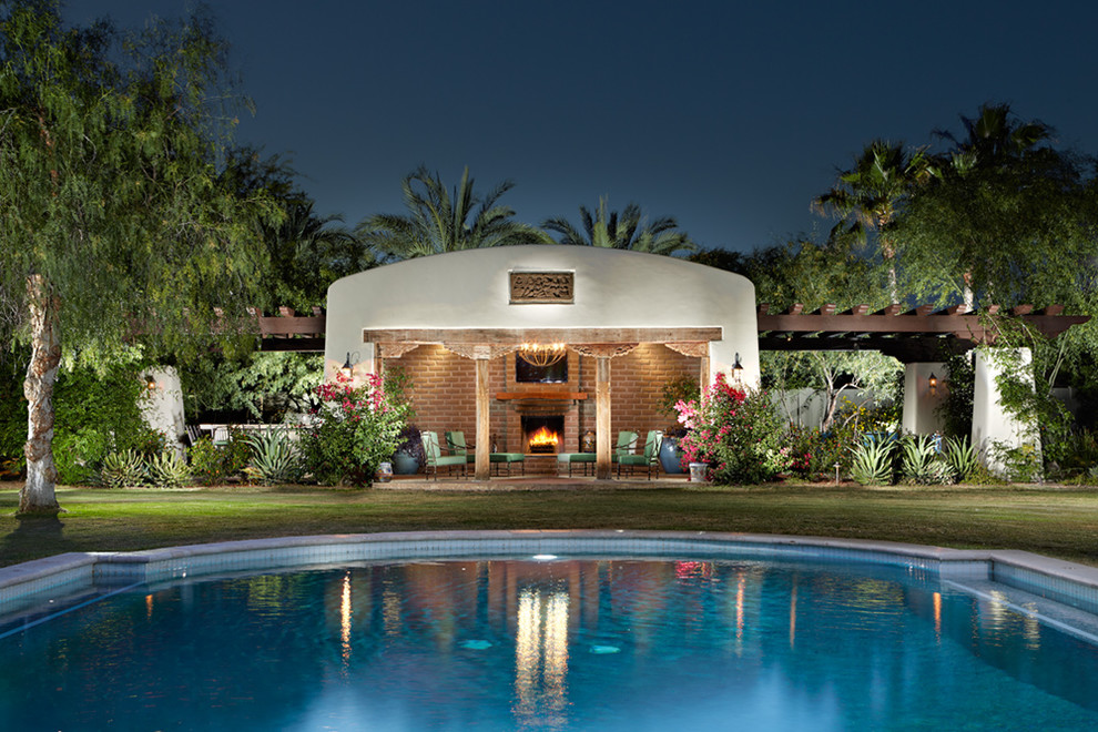 This is an example of a mid-sized backyard custom-shaped aboveground pool in Phoenix with a pool house and natural stone pavers.