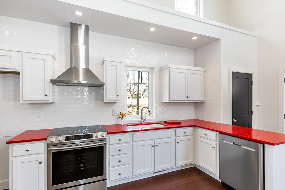 This is an example of a mid-sized modern l-shaped kitchen in Kansas City with an undermount sink, recessed-panel cabinets, white cabinets, quartz benchtops, white splashback, ceramic splashback, stainless steel appliances, bamboo floors, brown floor and red benchtop.