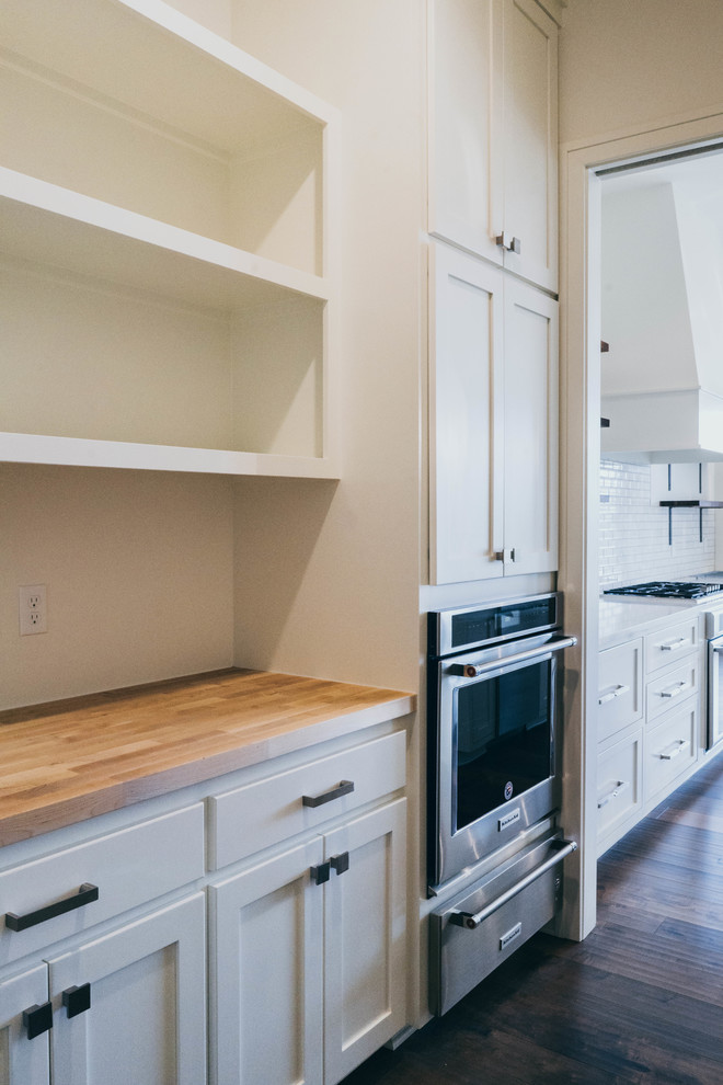 Example of a transitional dark wood floor kitchen pantry design in Omaha with a farmhouse sink, shaker cabinets, white cabinets, quartz countertops, paneled appliances and an island