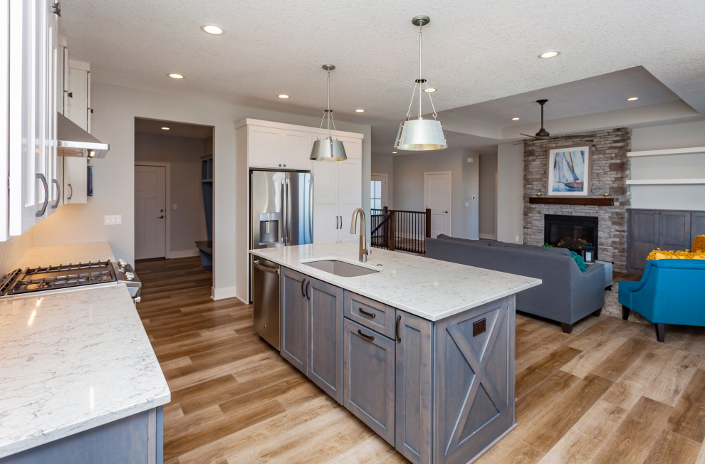 Inspiration for a mid-sized transitional l-shaped light wood floor and brown floor open concept kitchen remodel with an undermount sink, shaker cabinets, white cabinets, quartz countertops, white backsplash, ceramic backsplash, stainless steel appliances, an island and white countertops