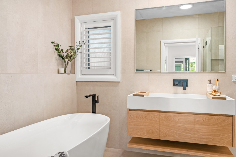Inspiration for a mid-sized beach style master bathroom in Central Coast with light wood cabinets, a freestanding tub, a corner shower, beige tile, an integrated sink, a hinged shower door, white benchtops, a single vanity and a floating vanity.