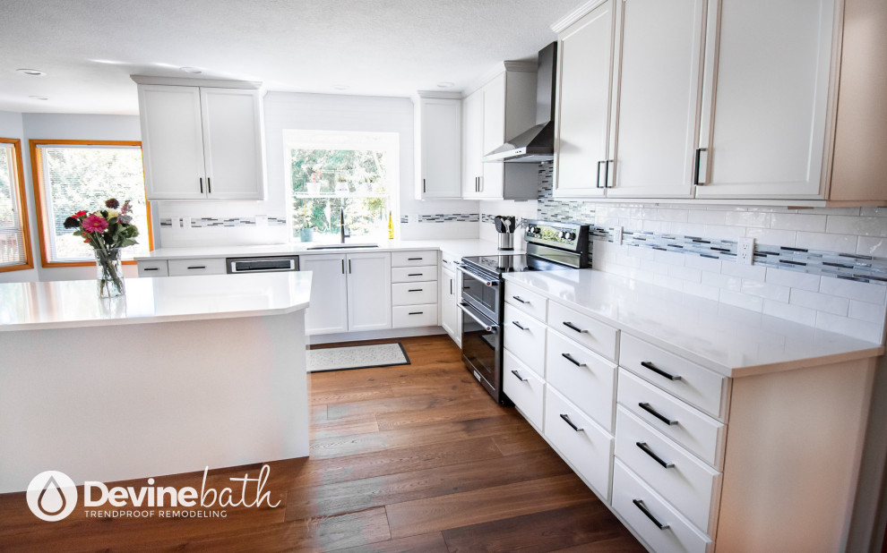 Open concept kitchen - large transitional l-shaped medium tone wood floor open concept kitchen idea in Portland with an undermount sink, recessed-panel cabinets, white cabinets, quartz countertops, white backsplash, glass tile backsplash, stainless steel appliances, an island and white countertops