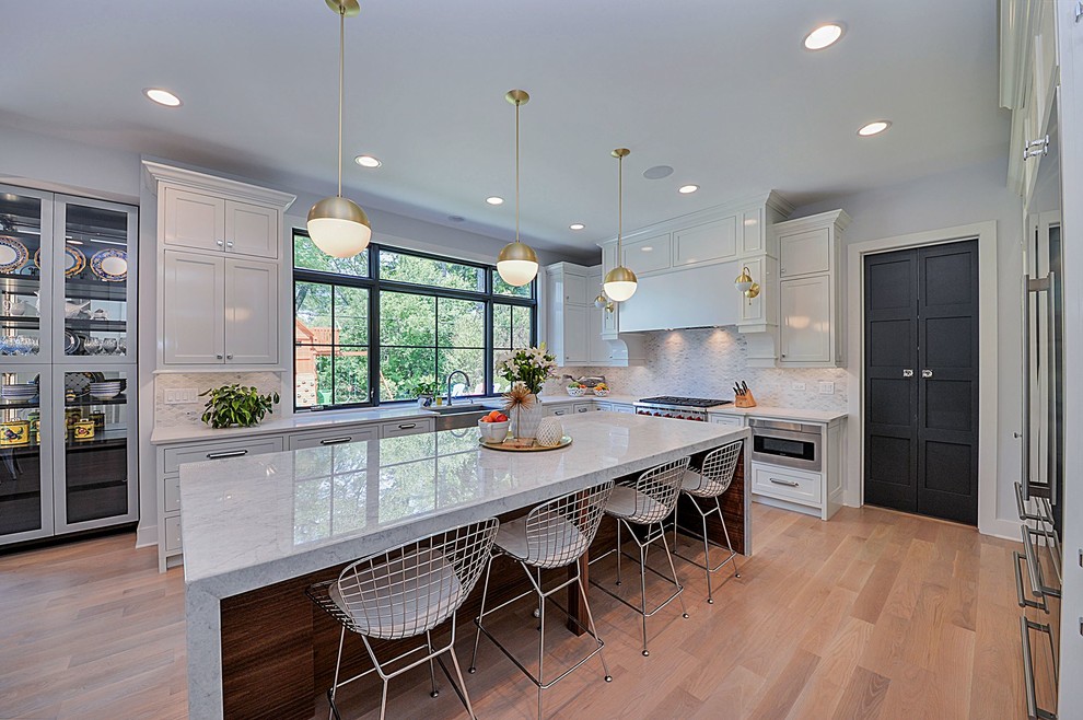 Inspiration for a mid-sized transitional u-shaped light wood floor eat-in kitchen remodel in Chicago with white cabinets, a farmhouse sink, recessed-panel cabinets, marble countertops, gray backsplash, mosaic tile backsplash, stainless steel appliances and an island
