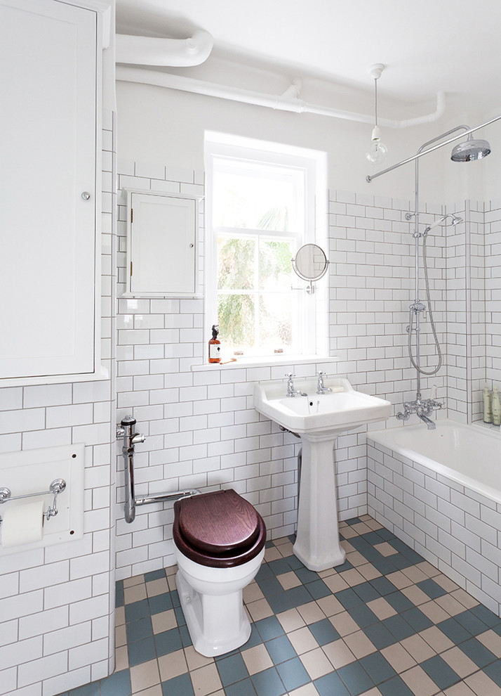 Industrial bathroom in Auckland with a drop-in tub, a shower/bathtub combo, a one-piece toilet, subway tile, white walls, a pedestal sink and a shower curtain.