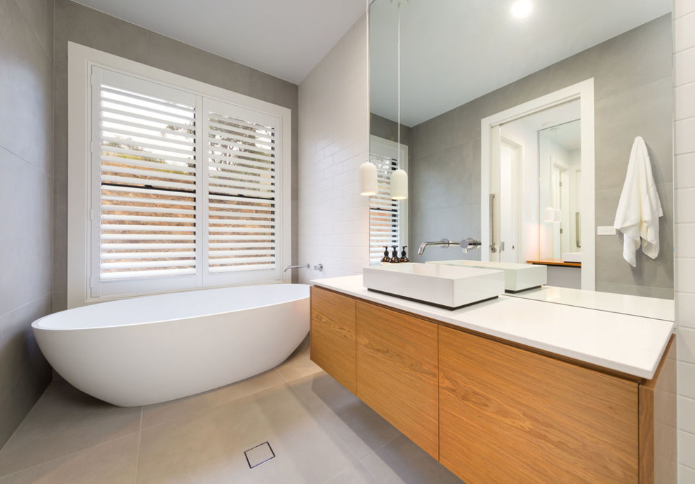 This is an example of a mid-sized contemporary kids bathroom with light wood cabinets, a freestanding tub, gray tile, porcelain tile, white walls, porcelain floors, engineered quartz benchtops, white floor and white benchtops.